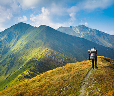 hiker trekking along a mountain trail with a large backpack surrounded by lush green hills and peaks ideal for outdoor adventures and exploring 16 outdoor experiences