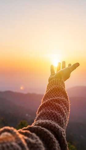 person reaching out towards sunset with warm colors in the sky highlighting 11 nature's beauty